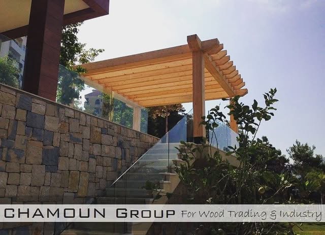 Timber pergola — An exterior structure over a terrace, on a stone retaining wall.